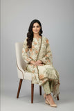 A woman sits on a cream upholstered chair wearing a light beige embroidered traditional outfit with floral print, matching pants, and beige heels against a light gray studio background.